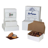 White bakery boxes shown on a white background, including closed boxes with printed labels and an open box containing chocolate donuts. Two glazed donuts and a powdered donut sit in front of the boxes.