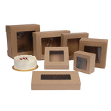 Brown Kraft bakery boxes with clear plastic window cutouts in various sizes, shown on a white background with a small white frosted cake beside one box.