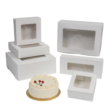 White bakery cake boxes with clear window cutouts, shown in various sizes and configurations on a white background, with a small white frosted cake placed in front.